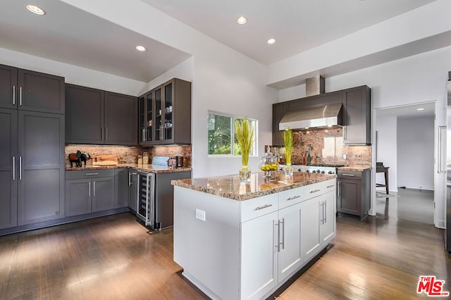 kitchen featuring light stone countertops, wine cooler, wall chimney exhaust hood, white cabinetry, and a kitchen island