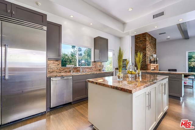 kitchen featuring light stone countertops, white cabinetry, stainless steel appliances, light hardwood / wood-style flooring, and a kitchen island