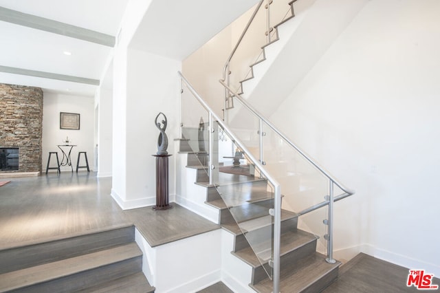 staircase featuring a stone fireplace and wood-type flooring