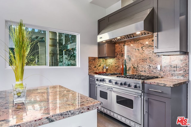 kitchen featuring decorative backsplash, double oven range, gray cabinetry, and wall chimney range hood