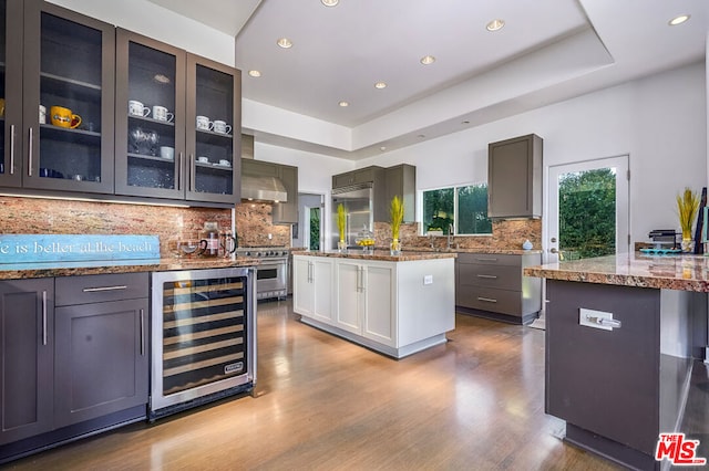 kitchen with gray cabinetry, wine cooler, light hardwood / wood-style flooring, a tray ceiling, and a kitchen island