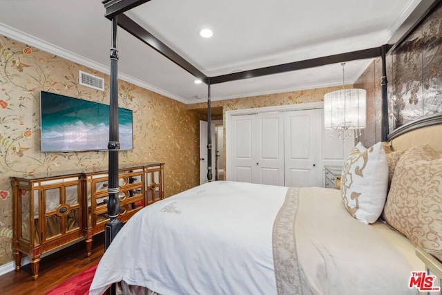 bedroom with a closet, an inviting chandelier, dark wood-type flooring, and ornamental molding