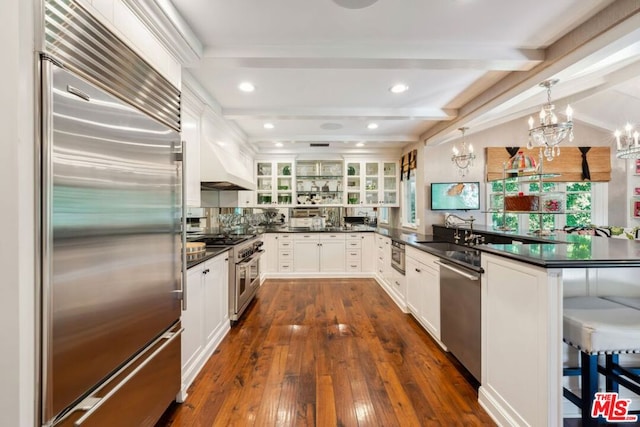 kitchen featuring premium appliances, sink, beam ceiling, decorative light fixtures, and white cabinets