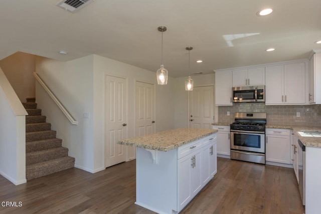 kitchen with decorative light fixtures, stainless steel appliances, a center island, and white cabinets