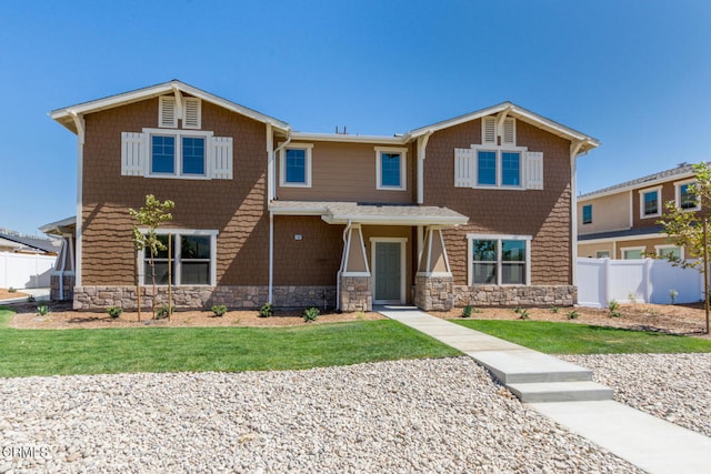 craftsman-style house featuring stone siding, fence, and a front lawn