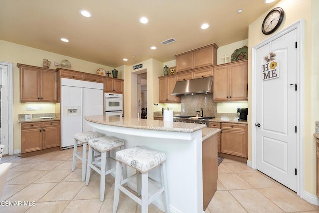 kitchen with paneled fridge, light stone counters, a kitchen bar, a center island with sink, and light tile patterned flooring