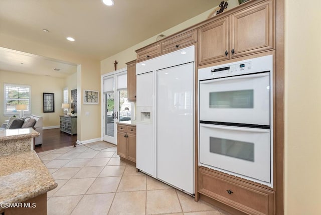 kitchen featuring light stone countertops, light tile patterned floors, white double oven, and paneled built in fridge