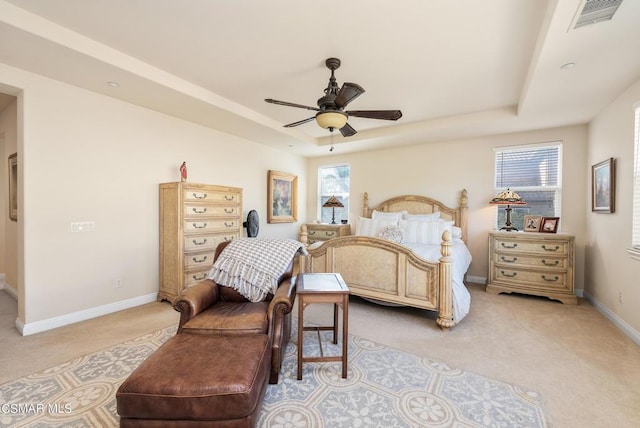 carpeted bedroom with a tray ceiling, multiple windows, and ceiling fan