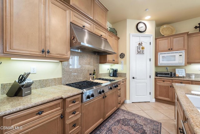 kitchen featuring stainless steel gas stovetop, backsplash, white microwave, light tile patterned floors, and light stone counters