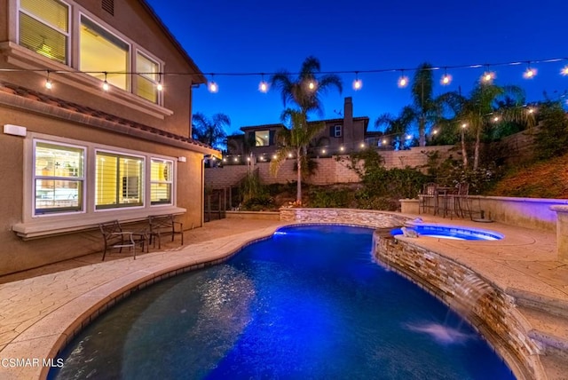 pool at twilight with pool water feature, a patio area, and an in ground hot tub