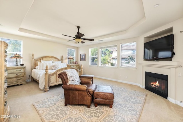 carpeted bedroom with multiple windows, a tray ceiling, and ceiling fan