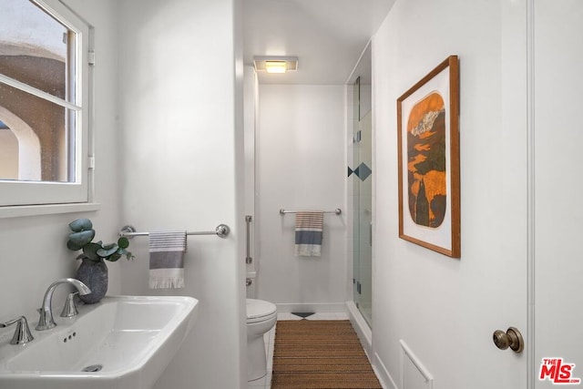 bathroom featuring a shower with door, toilet, a wealth of natural light, and sink