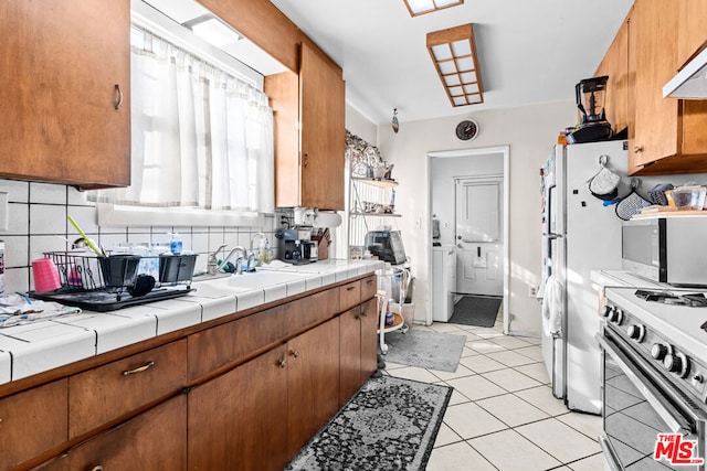 kitchen featuring light tile patterned floors, sink, washer and clothes dryer, white gas range oven, and tile counters