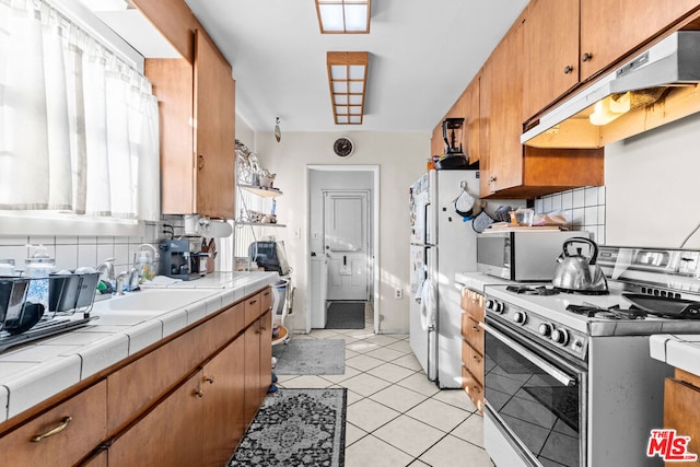 kitchen featuring sink, white appliances, light tile patterned floors, backsplash, and tile counters