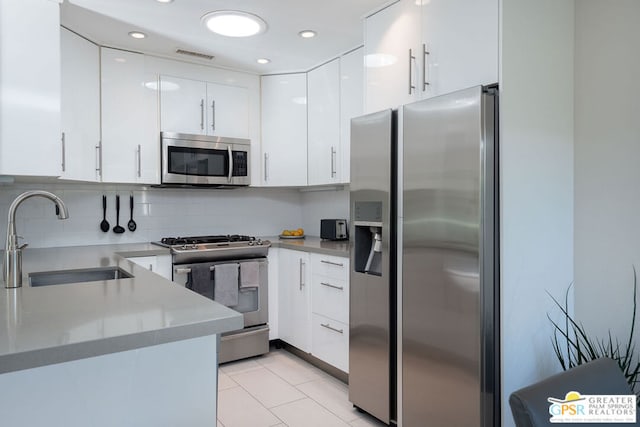 kitchen with sink, decorative backsplash, light tile patterned floors, appliances with stainless steel finishes, and white cabinetry