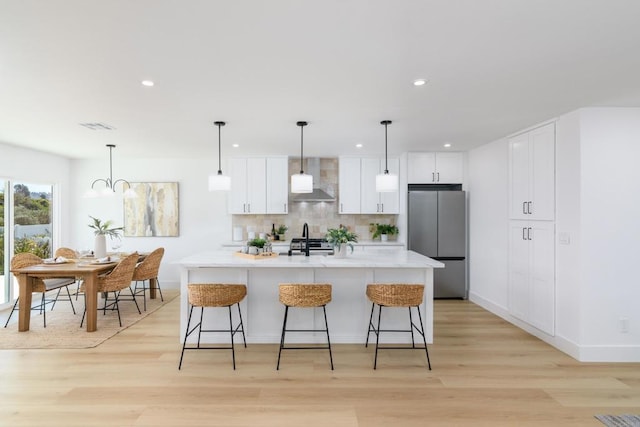 kitchen with appliances with stainless steel finishes, hanging light fixtures, an island with sink, light hardwood / wood-style floors, and decorative backsplash