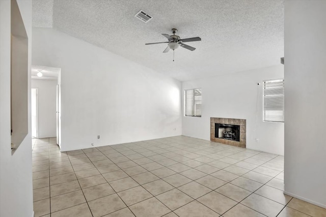 unfurnished living room featuring vaulted ceiling, ceiling fan, a fireplace, a textured ceiling, and light tile patterned flooring