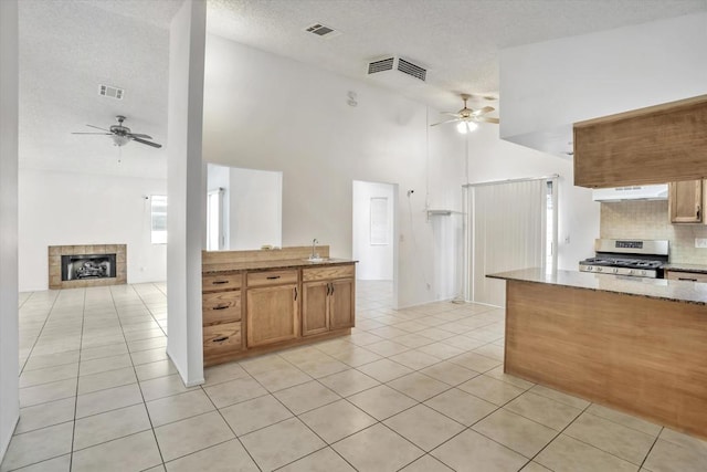 kitchen featuring a towering ceiling, light tile patterned flooring, a tile fireplace, and stainless steel gas range