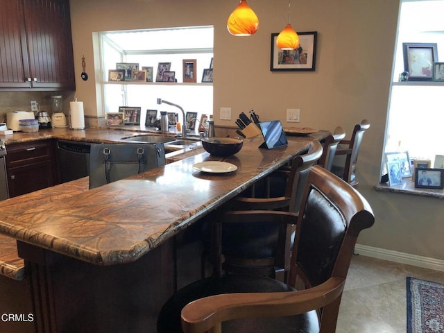 kitchen featuring dishwasher, hanging light fixtures, dark brown cabinets, kitchen peninsula, and a breakfast bar area