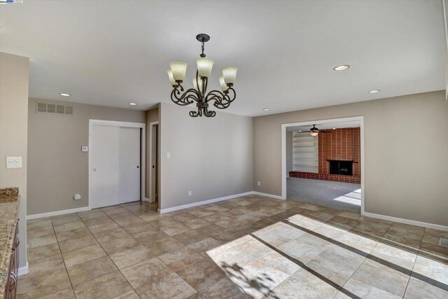 spare room with a brick fireplace and ceiling fan with notable chandelier