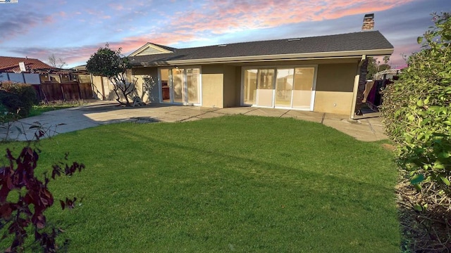 back house at dusk featuring a patio area and a yard