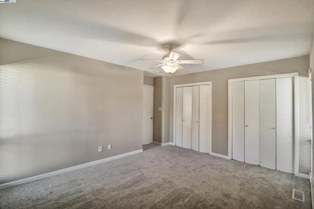 unfurnished bedroom with ceiling fan, carpet floors, and multiple closets