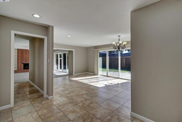 unfurnished room featuring a brick fireplace, a notable chandelier, and light tile patterned flooring