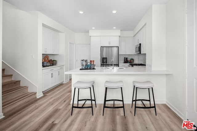 kitchen with tasteful backsplash, kitchen peninsula, a breakfast bar, white cabinets, and appliances with stainless steel finishes