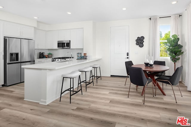 kitchen featuring kitchen peninsula, stainless steel appliances, white cabinetry, and light hardwood / wood-style flooring