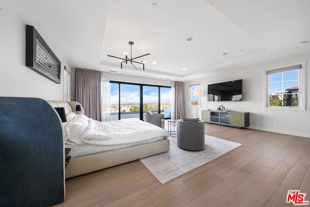 bedroom with light hardwood / wood-style floors, multiple windows, a raised ceiling, and a chandelier