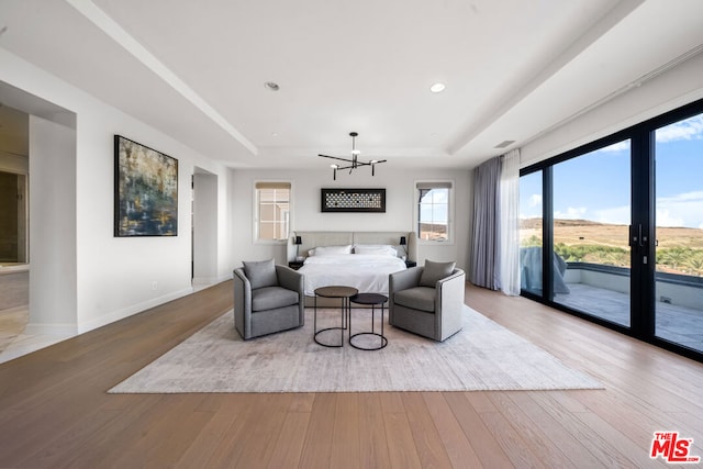 bedroom featuring an inviting chandelier, hardwood / wood-style floors, access to outside, and a tray ceiling