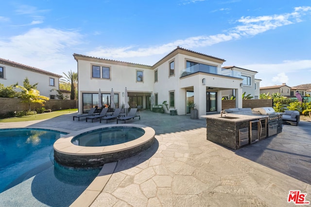 rear view of property featuring a fire pit, a balcony, a swimming pool with hot tub, and a patio area