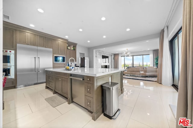 kitchen featuring stainless steel appliances, a notable chandelier, light tile patterned floors, a kitchen island with sink, and sink