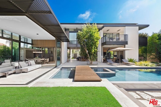 rear view of house featuring a pool with hot tub, an outdoor living space, a balcony, and a patio