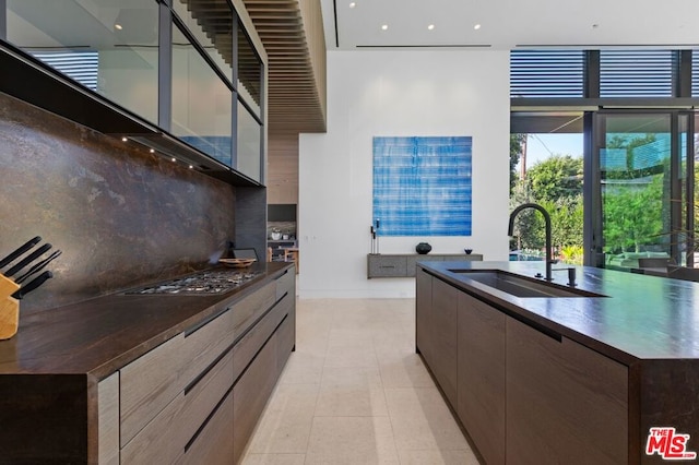 kitchen with stainless steel gas stovetop, decorative backsplash, sink, an island with sink, and light tile patterned floors