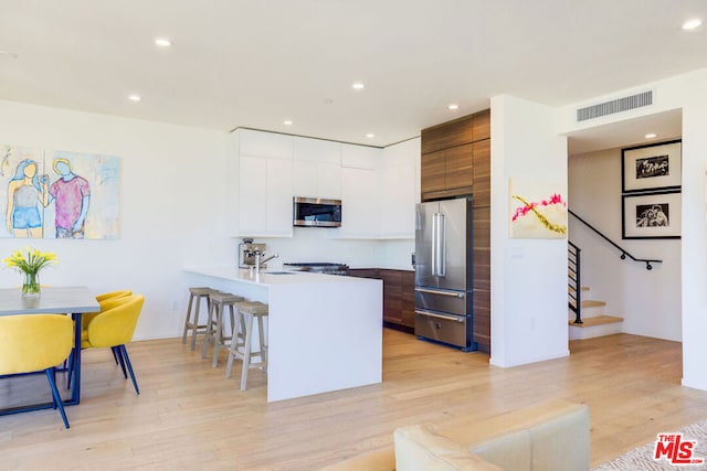 kitchen featuring a breakfast bar, white cabinets, stainless steel appliances, and light hardwood / wood-style floors