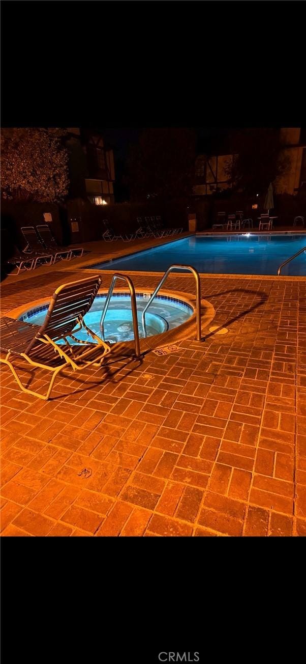 pool at twilight with a hot tub, a community pool, and a patio