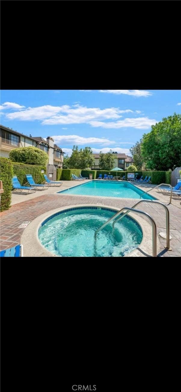 pool with a patio area and a hot tub