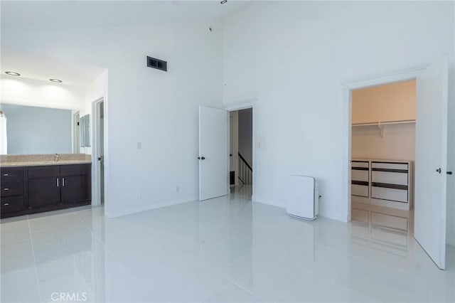 unfurnished bedroom with light tile patterned floors, high vaulted ceiling, a sink, visible vents, and a spacious closet