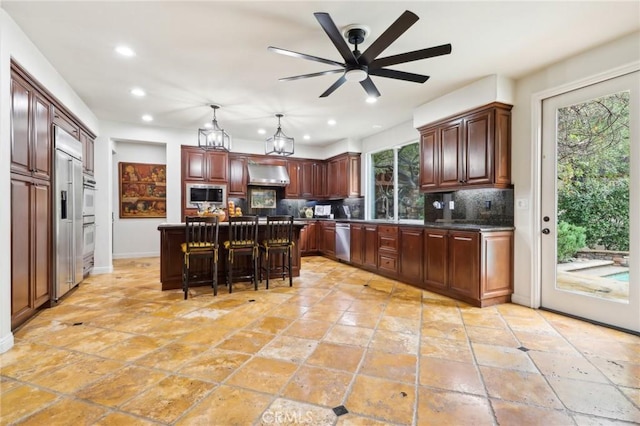 kitchen with wall chimney range hood, a breakfast bar, a center island, built in microwave, and stainless steel dishwasher