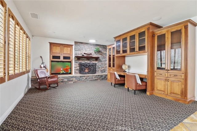 carpeted home office with a stone fireplace and built in desk