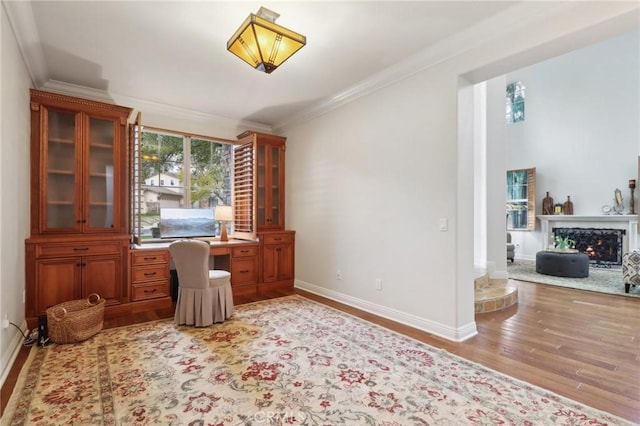 home office with crown molding, a fireplace, built in desk, and light hardwood / wood-style flooring