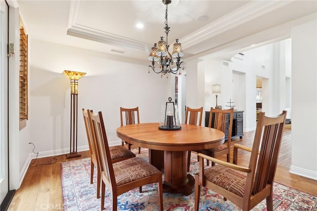 dining room with wood-type flooring, a notable chandelier, crown molding, and a tray ceiling