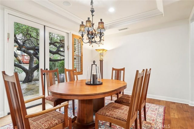 dining space featuring hardwood / wood-style flooring, ornamental molding, a raised ceiling, and a chandelier