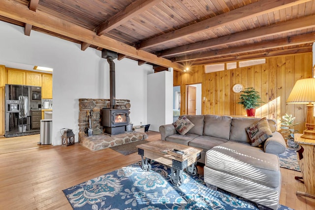 living room featuring wood walls, a wood stove, light wood-type flooring, beamed ceiling, and wood ceiling