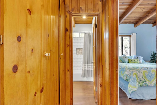 bedroom featuring beam ceiling, connected bathroom, wooden ceiling, and multiple windows