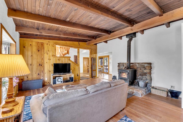 living room featuring a wood stove, wooden ceiling, wooden walls, beamed ceiling, and light hardwood / wood-style floors