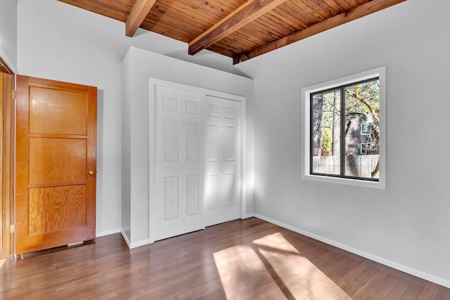 unfurnished bedroom with beam ceiling, dark hardwood / wood-style flooring, a closet, and wooden ceiling