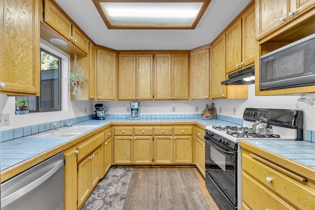 kitchen with tile counters, light hardwood / wood-style flooring, black appliances, and sink