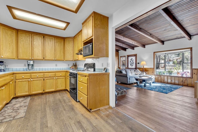 kitchen featuring range with gas stovetop, beamed ceiling, wooden walls, and light hardwood / wood-style flooring